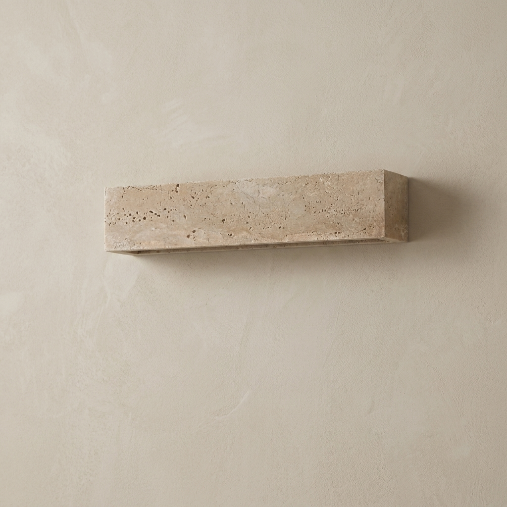 The Monolith travertine wall light, unlit, on a lime-washed plaster wall — Selden Home product photography