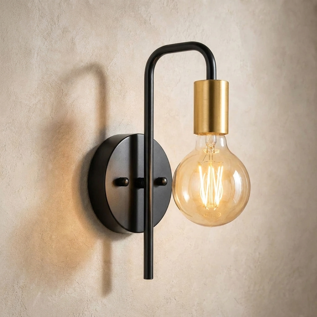 The Filament black and gold industrial wall sconce with exposed bulb, lit, mounted on a lime-washed plaster wall — Selden Home product photography