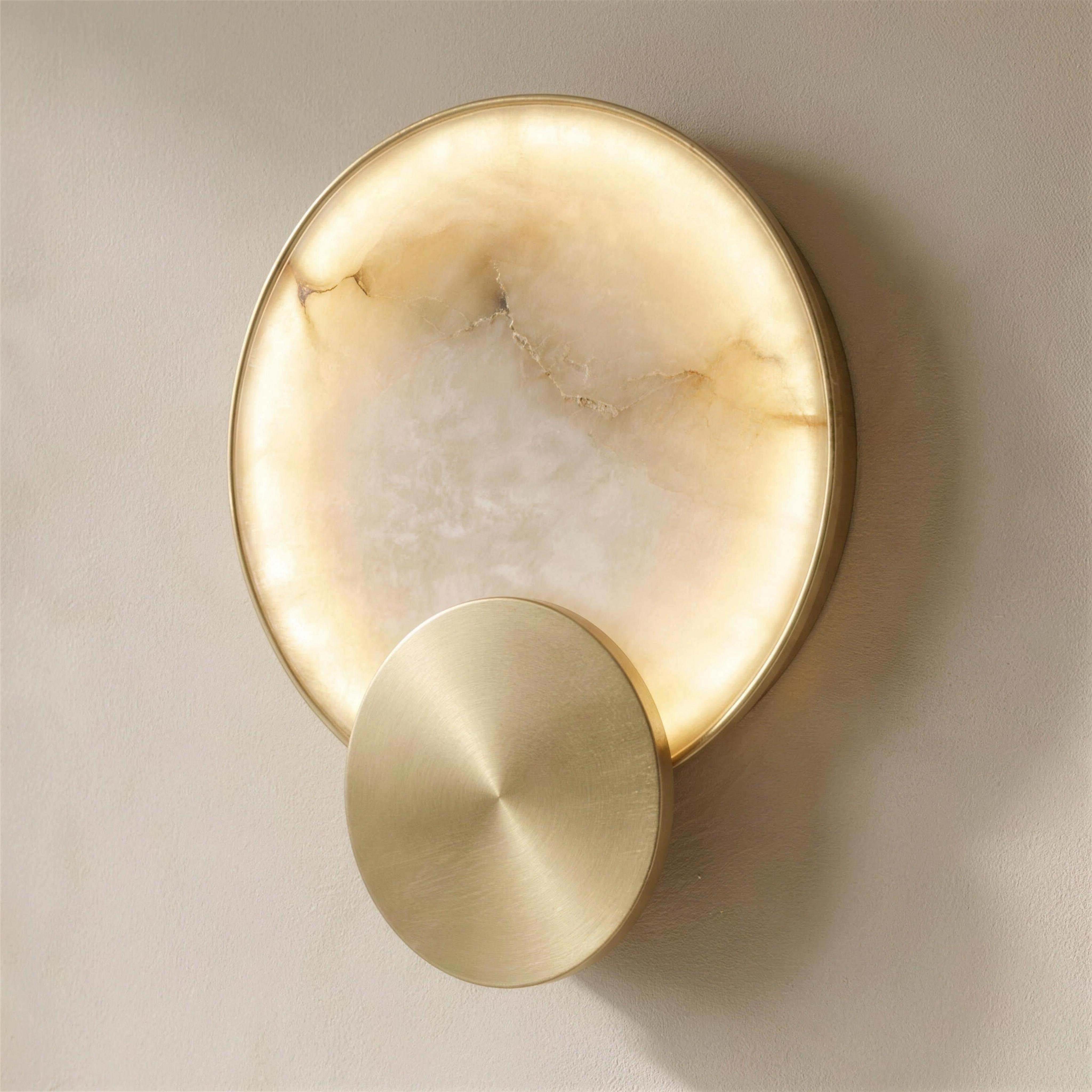 The Eclipse marble wall light at a three-quarter angle, lit, showing its depth against a lime-washed plaster wall — Selden Home product photography