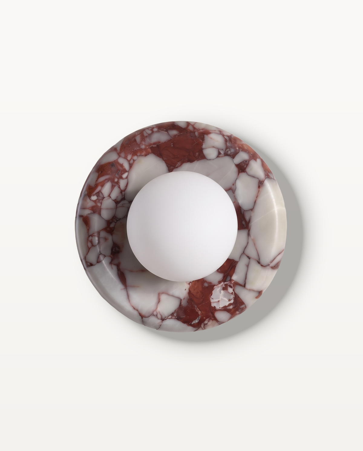 The Cameo Wall Light in Oxblood Breccia – a ring of oxblood and white breccia marble with a frosted glass globe, seen from the front