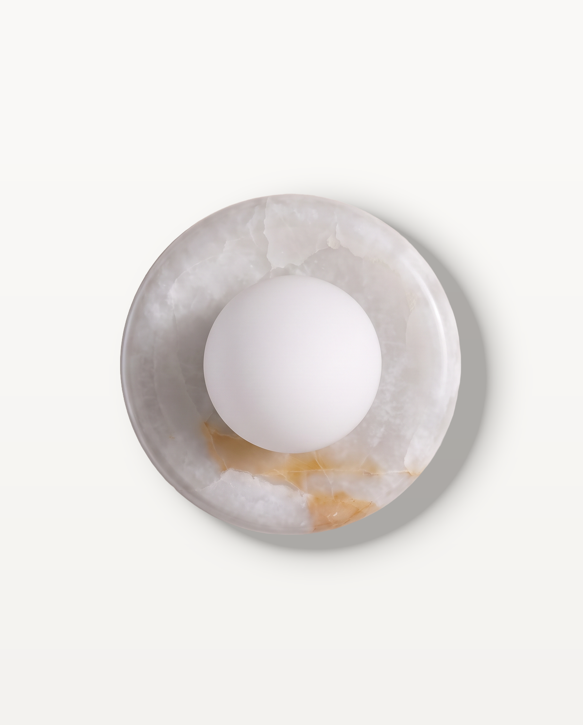 The Cameo Wall Light in White Onyx – a ring of white onyx with honey veining and a frosted glass globe, seen from the front