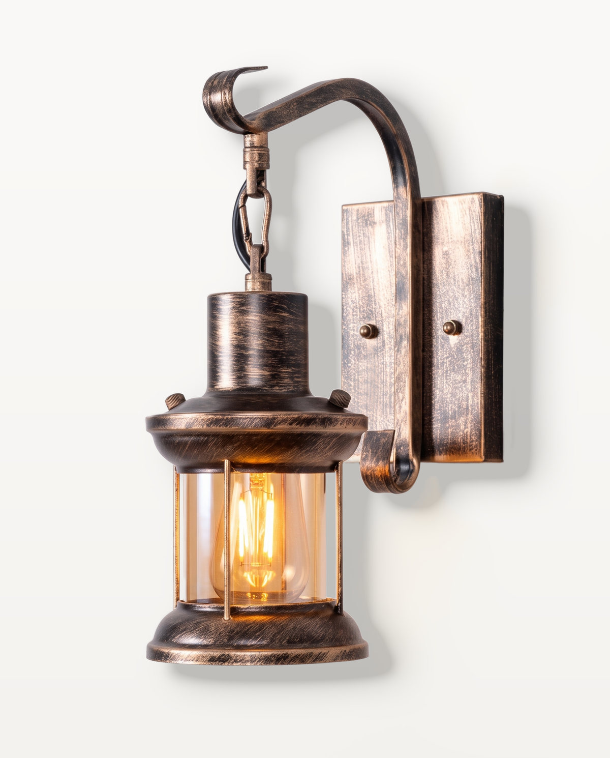 The Ostler Wall Light in Antique Bronze, a glass lantern on a hooked arm, lit