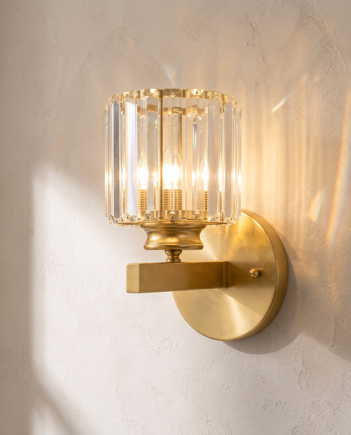 The Prism gold art deco crystal wall sconce, lit, mounted on a lime-washed plaster wall — Selden Home product photography