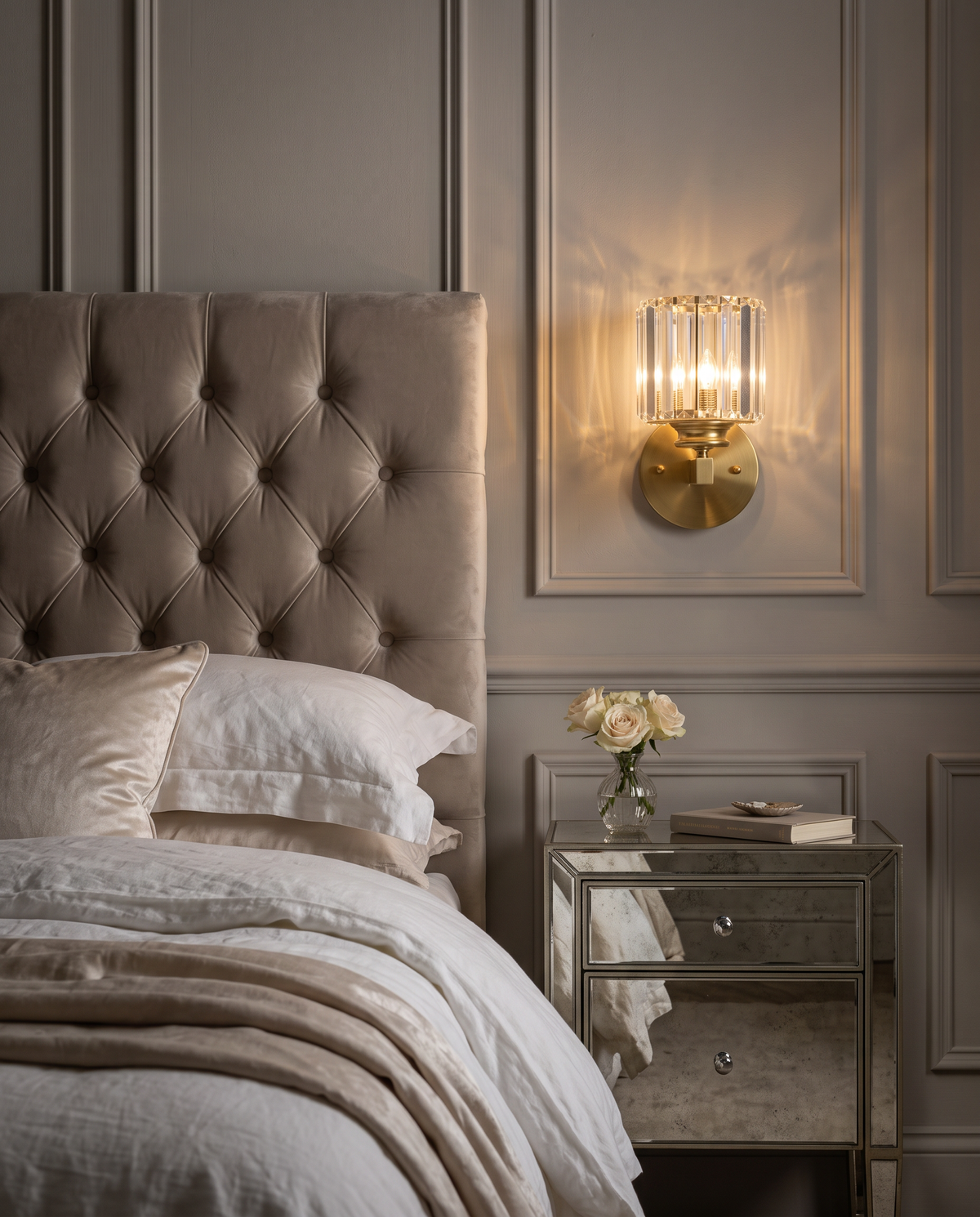 The Prism crystal wall sconce in brass beside a buttoned velvet headboard