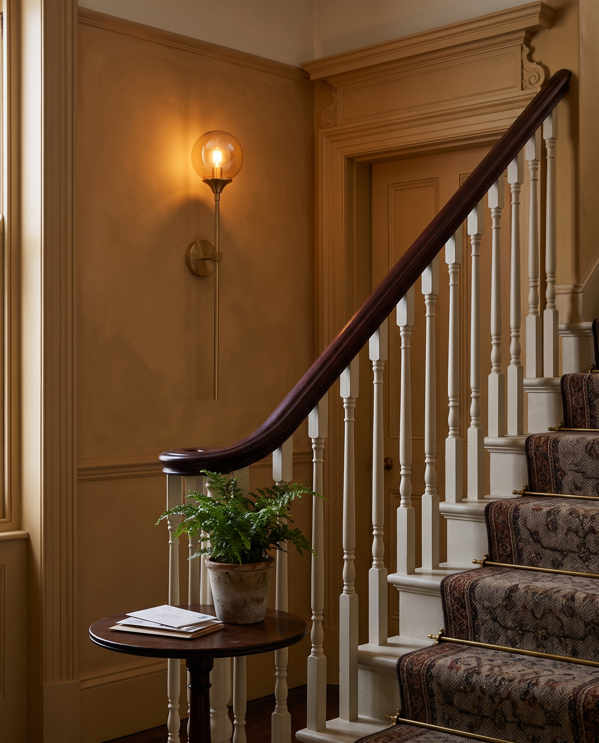 The Reed long-stem wall sconce in brass with an amber globe in a staircase hall
