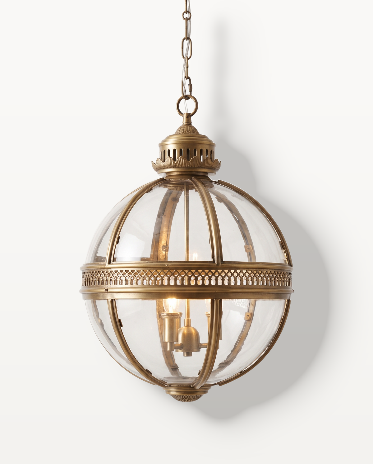 The Regent Pendant in Antique Gold, a clear glass globe in an open metal cage, lit