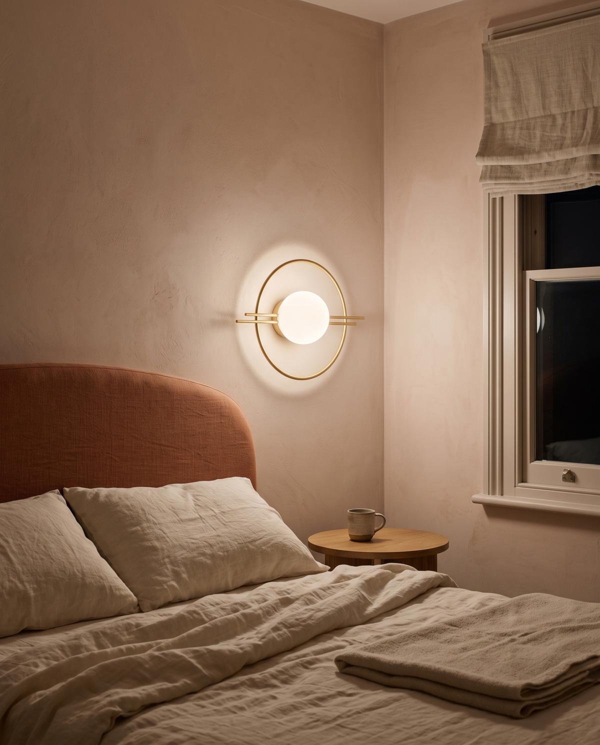 The Ring globe wall sconce in brass above a bedside table