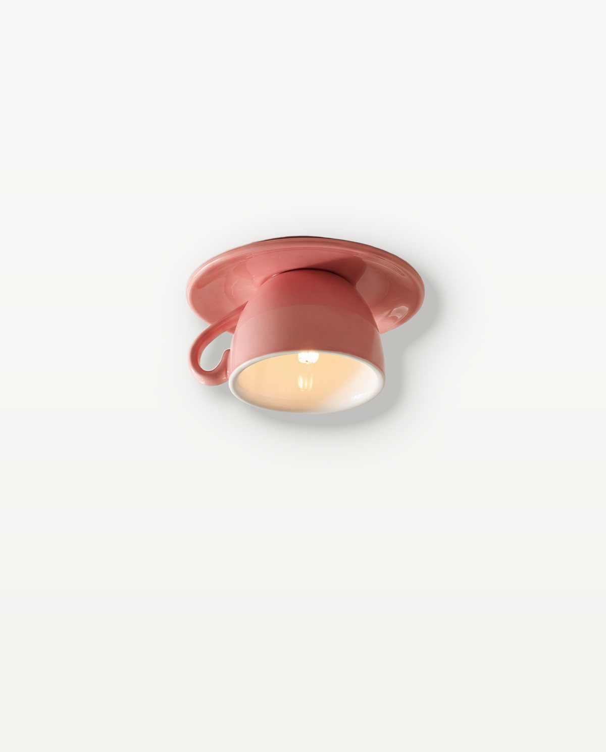 The Teacup Ceiling Light in Rhubarb, a glazed ceramic cup and saucer on the ceiling, lit