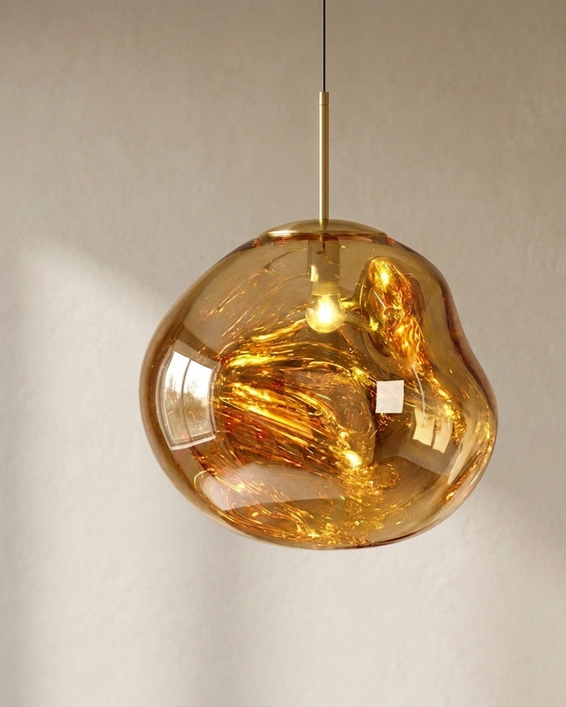 The Ember gold molten acrylic pendant light with brass fittings, lit, in front of a lime-washed plaster wall — Selden Home product photography