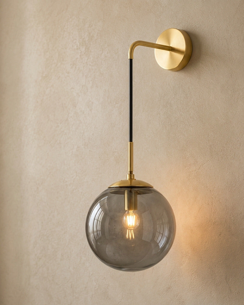 The Lantern, smoke grey glass wall sconce on gold hook arm, mounted on plaster wall — Selden Home product photography