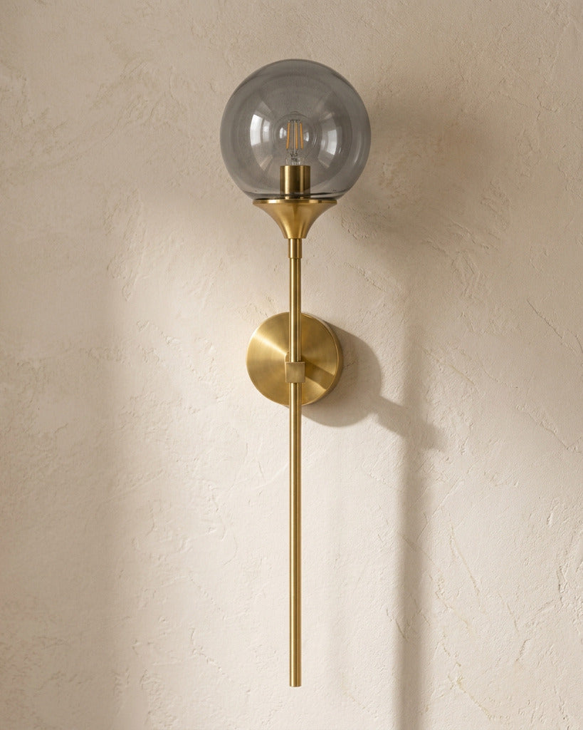 The Reed, gold long-stem wall sconce with smoke grey glass globe, mounted on plaster wall — Selden Home product photography