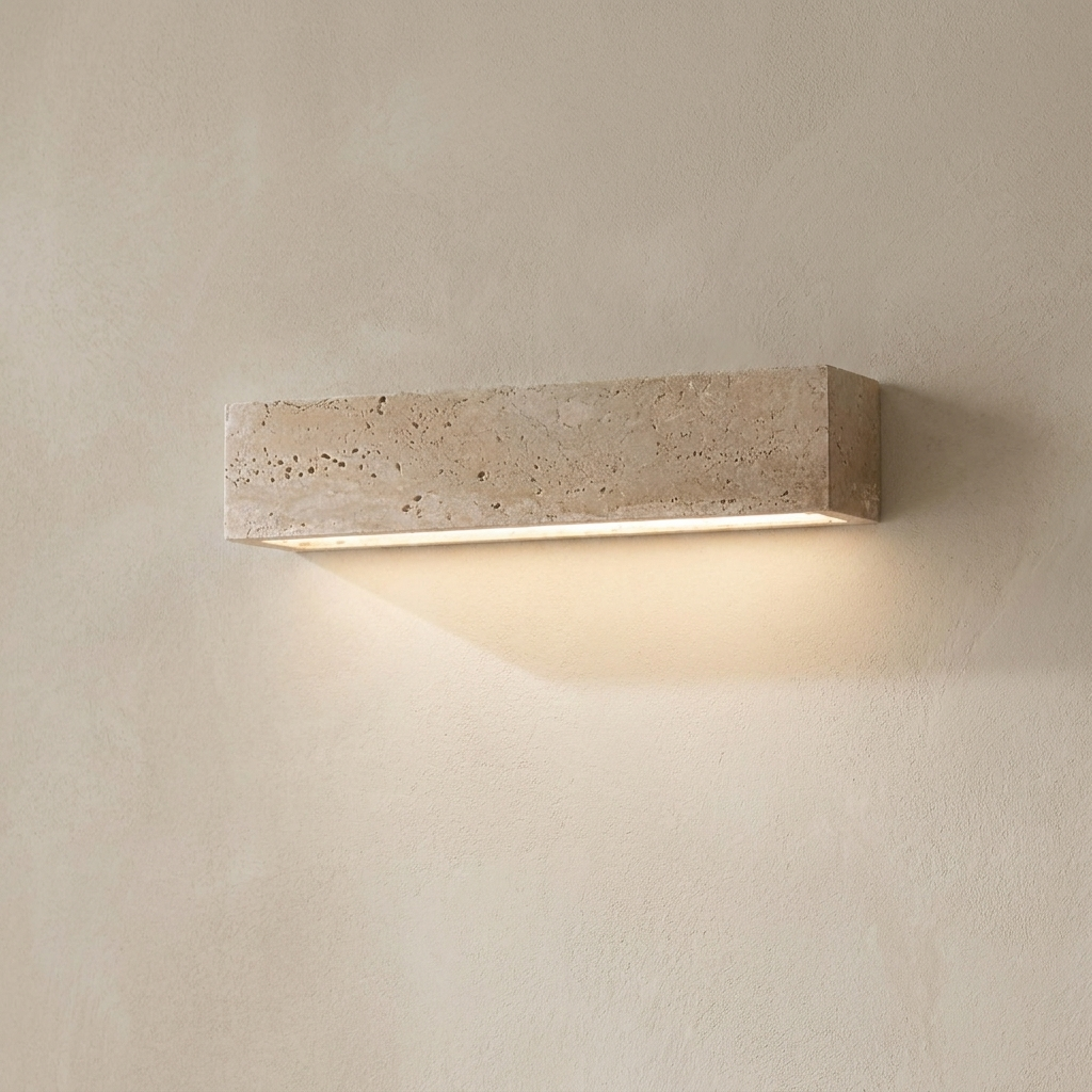 The Monolith travertine wall light, lit, on a lime-washed plaster wall — Selden Home product photography
