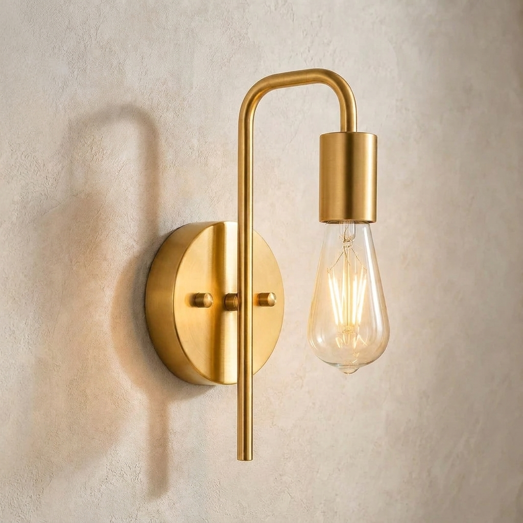 The Filament gold industrial wall sconce with exposed bulb, lit, mounted on a lime-washed plaster wall — Selden Home product photography