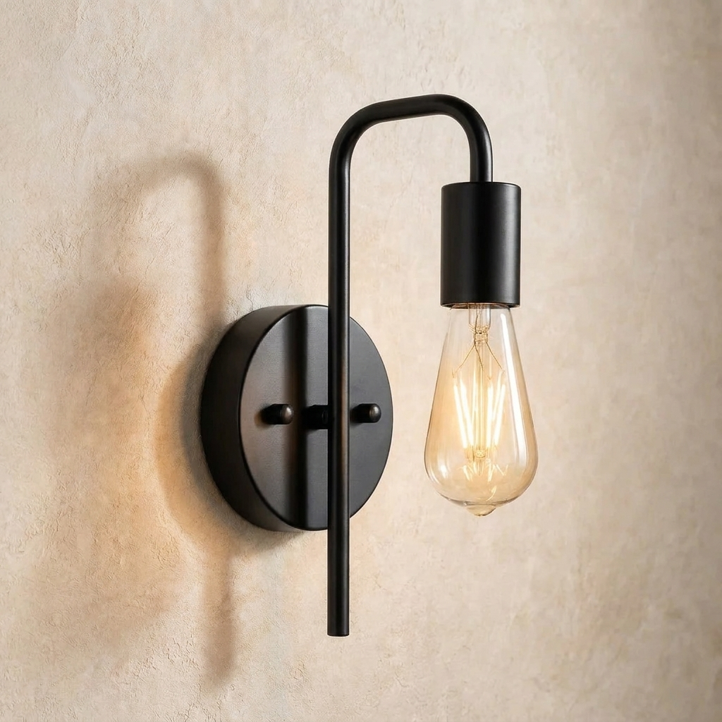 The Filament black industrial wall sconce with exposed bulb, lit, mounted on a lime-washed plaster wall — Selden Home product photography
