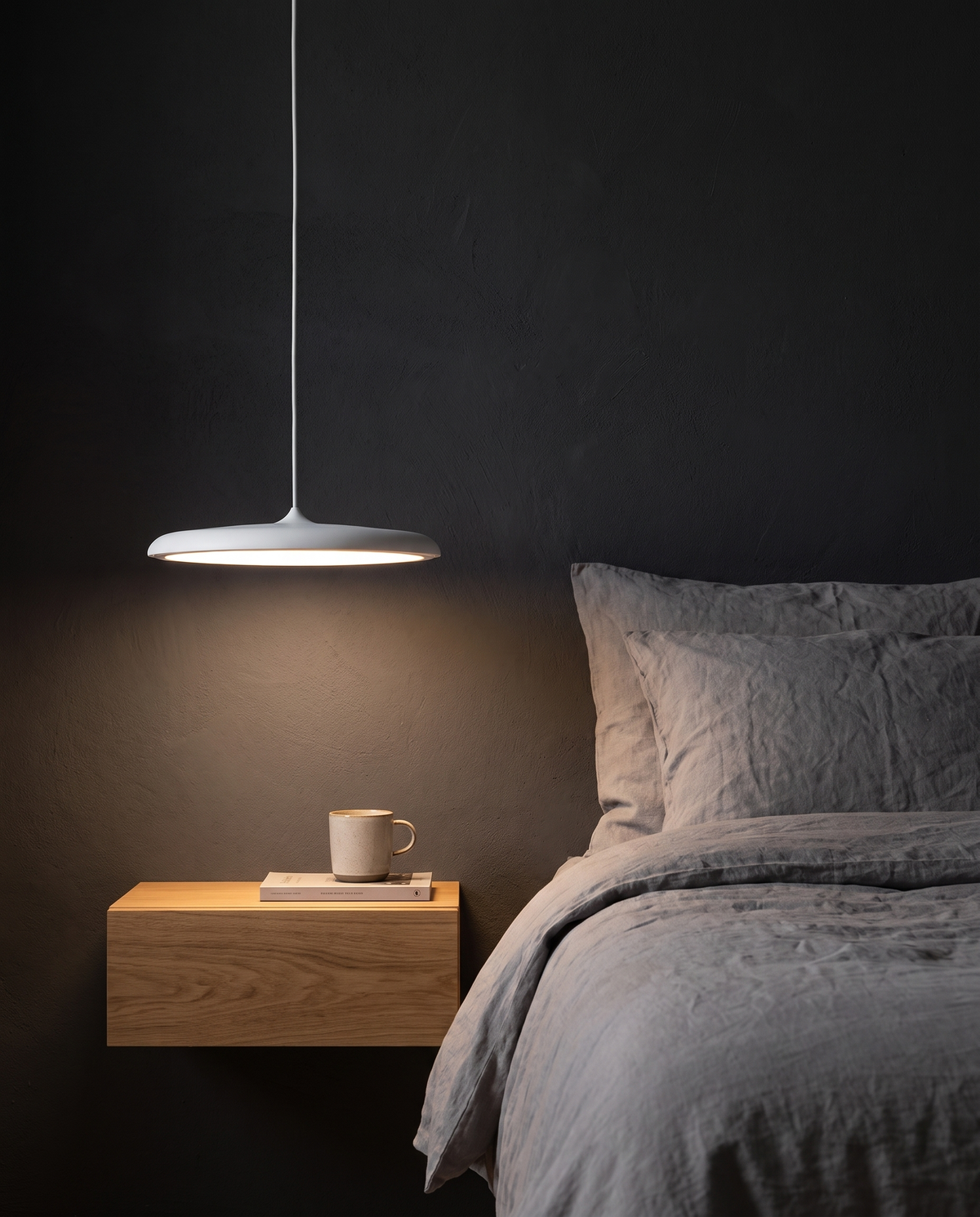 The Wafer Pendant in white as a bedside light against a charcoal wall
