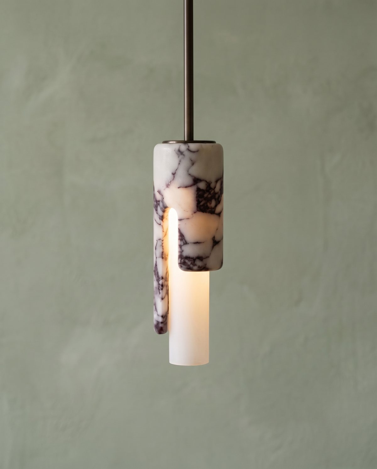 The Flute Pendant switched on in front of a sage green wall