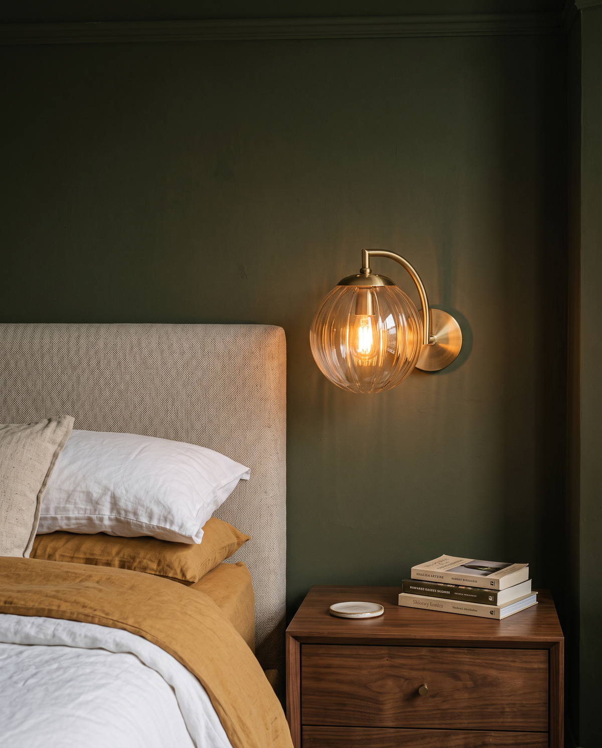 The Bloom wall sconce in amber ribbed glass beside a bed against an olive green wall