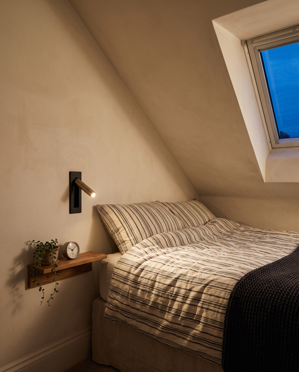 A Bookmark reading light above a bedside shelf in a guest room under the eaves