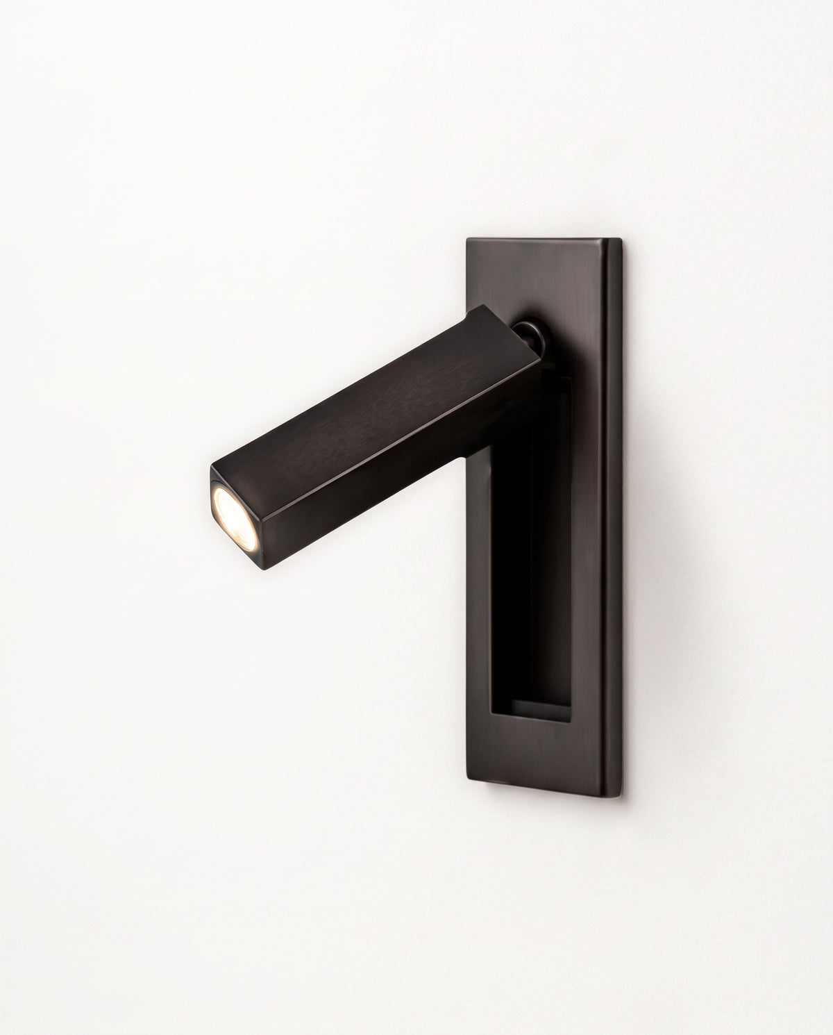 The Bookmark Wall Light in Jet with a square arm, swung out of its recessed wall plate, lit