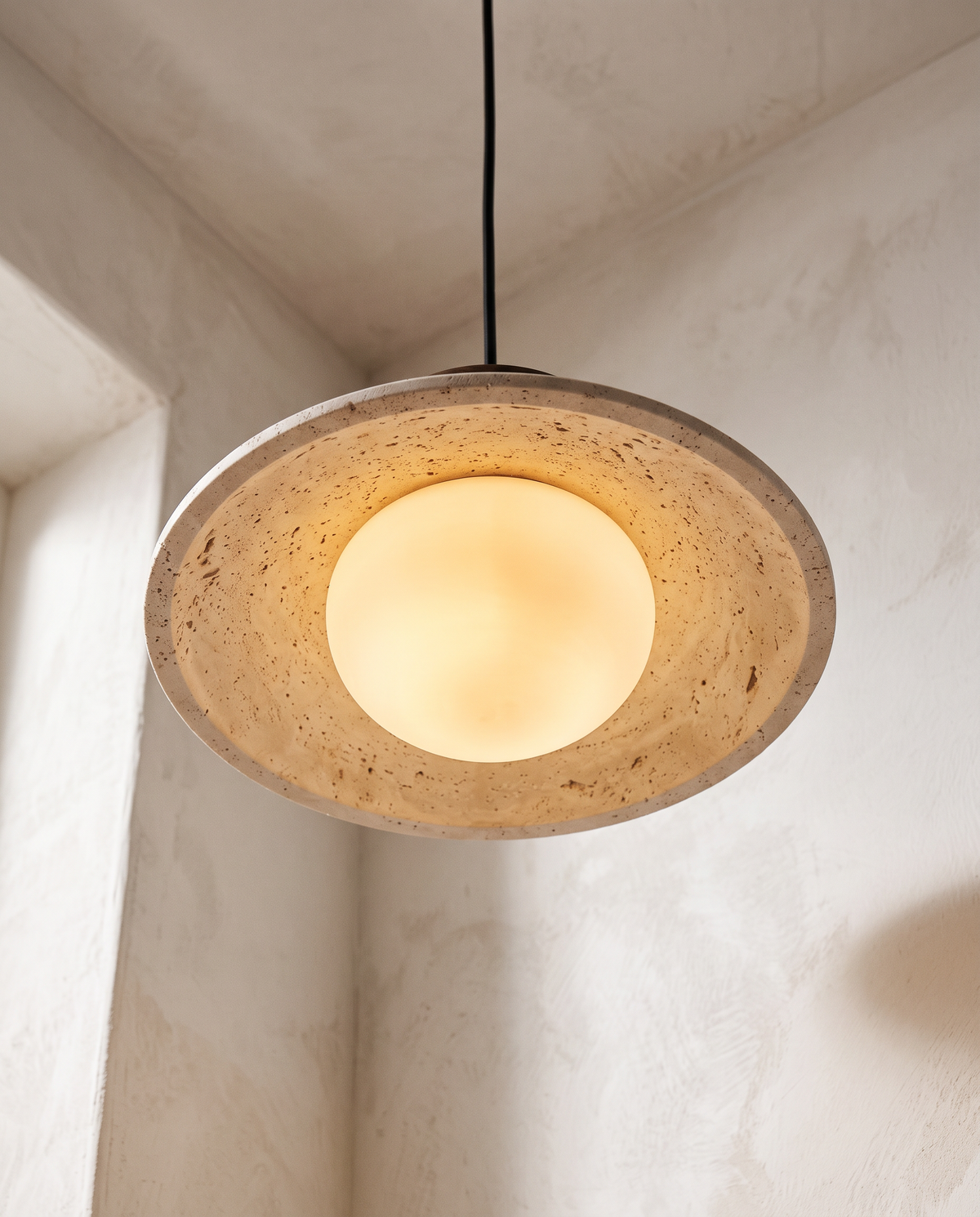 The opal globe glowing under the travertine shade of The Brim, seen from below