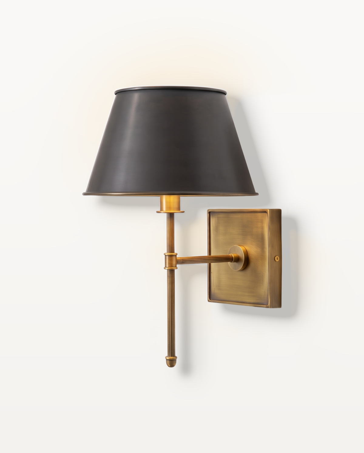 The Bureau Wall Light, a black shade on a fluted antiqued brass rod, lit