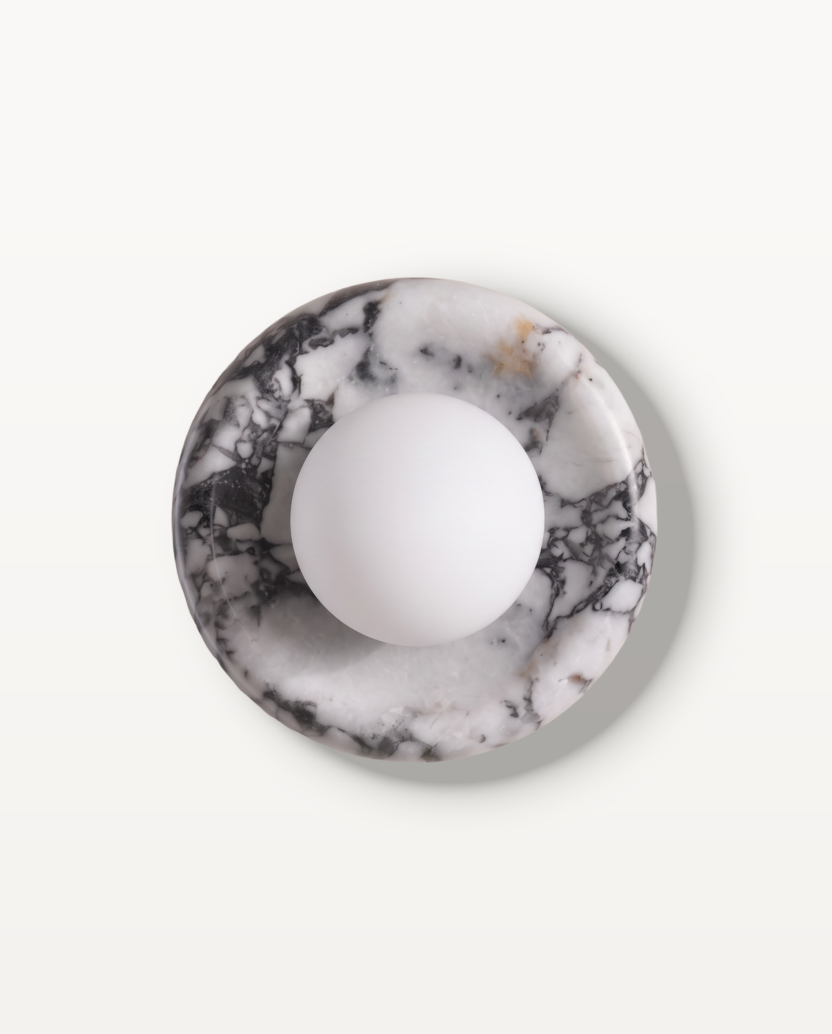 The Cameo Wall Light in Monochrome Breccia – a ring of black and white breccia marble with a frosted glass globe, seen from the front