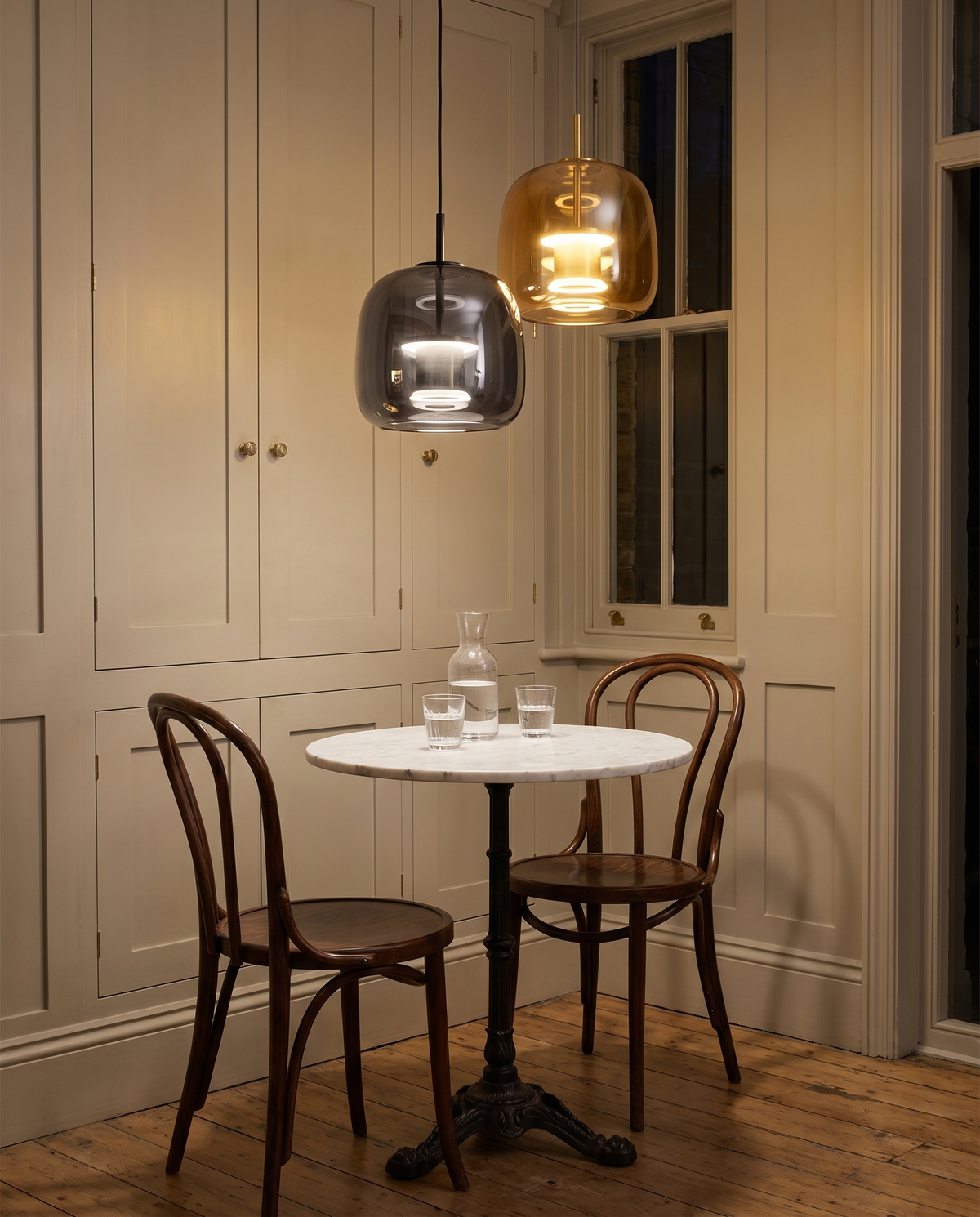 A smoked and an amber Capsule Pendant over a marble bistro table in a Victorian kitchen