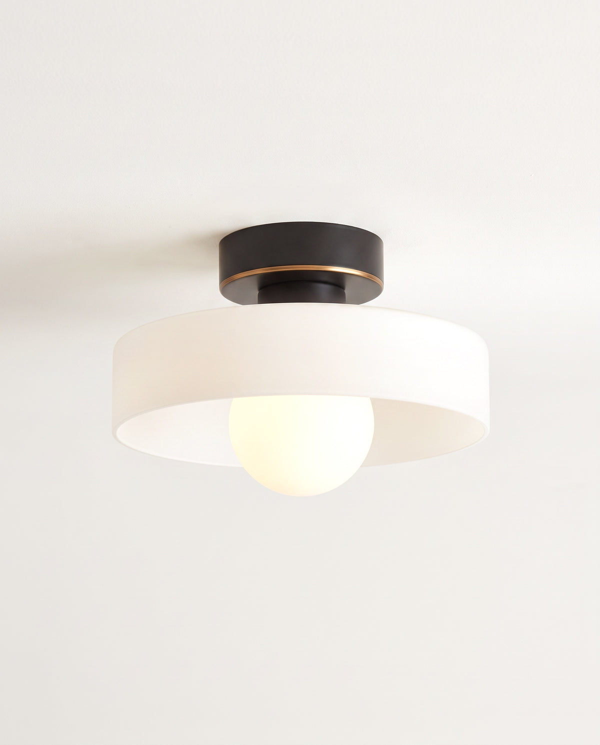 The Cloche Ceiling Light in Jet & Opal, a flat round glass shade under a black canopy, lit