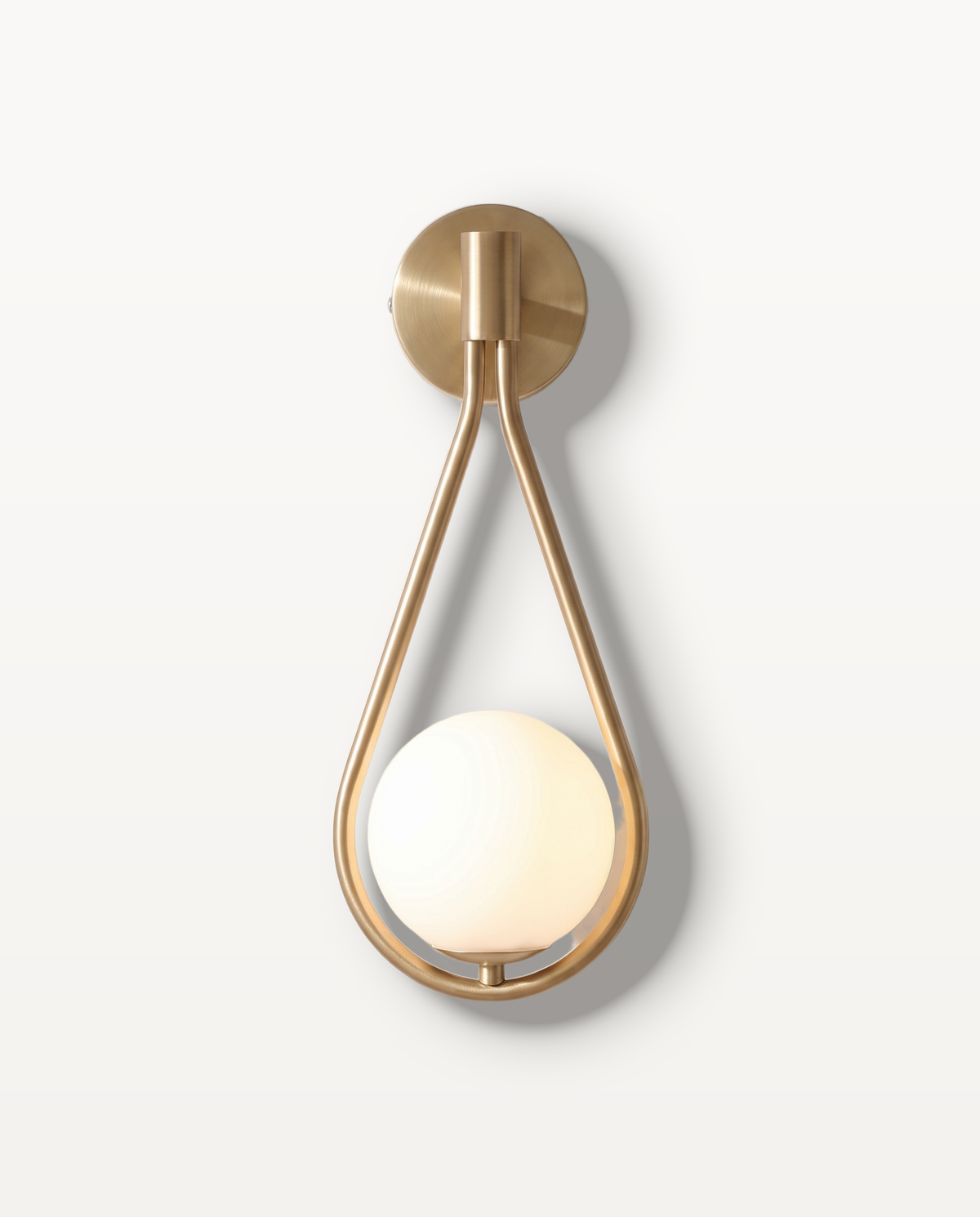 The Droplet Wall Light in brushed gold – a teardrop frame cradling an opal glass globe