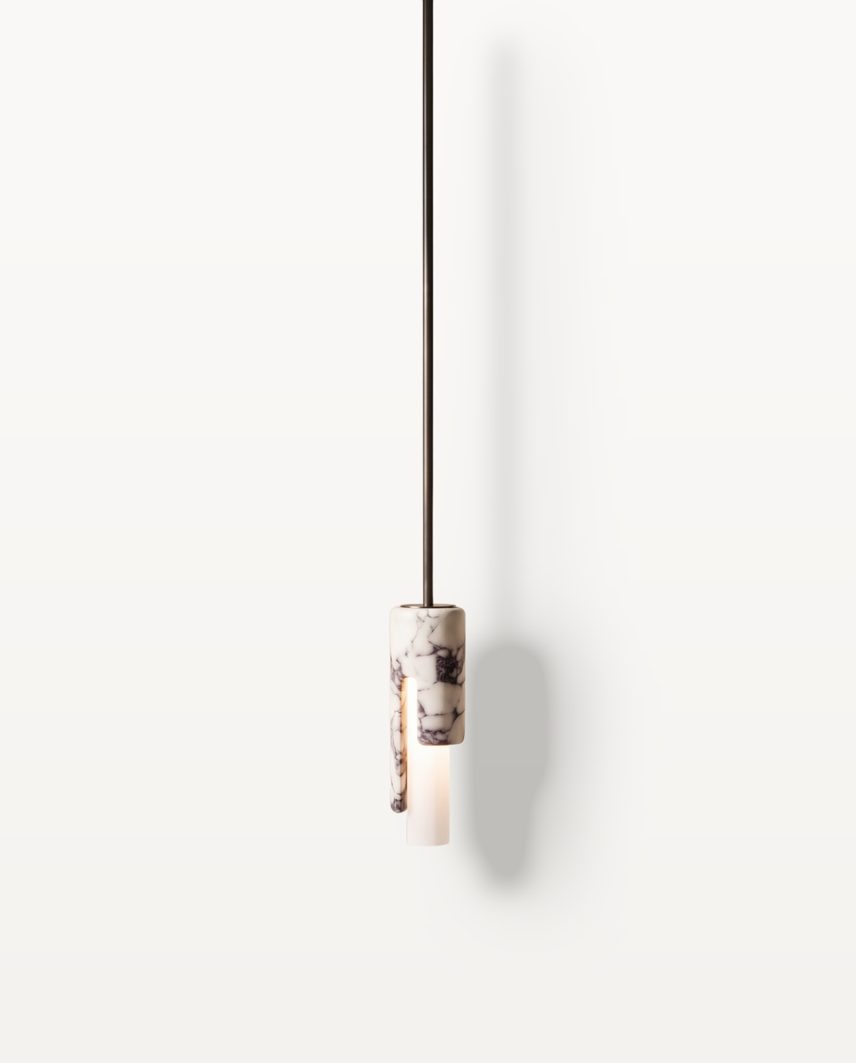 The Flute Pendant in veined marble, lit, against a limewashed plaster wall