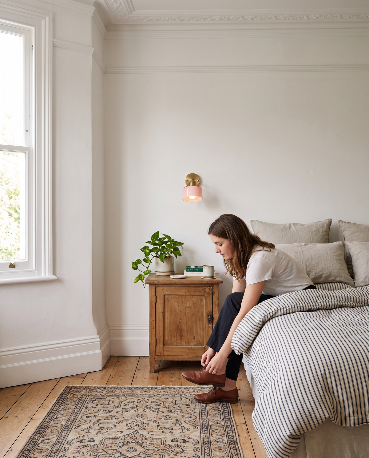 A young woman by the bed under an Inkwell wall light in Blush