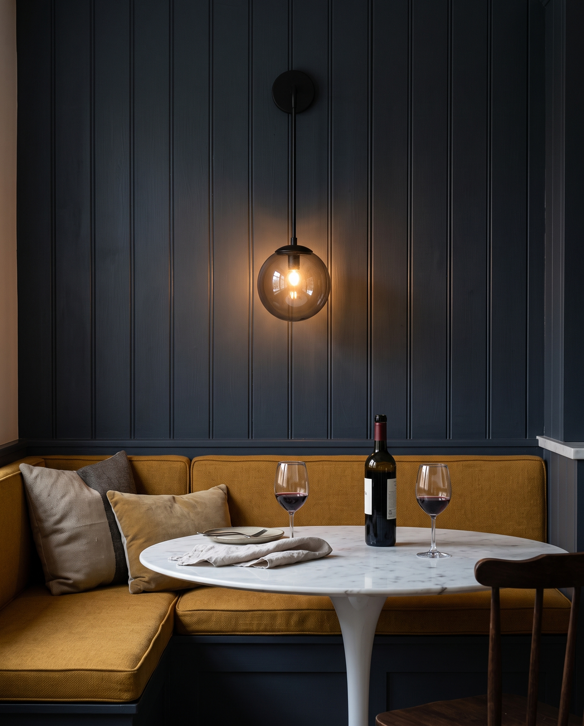 The Lantern wall light in black with a smoke grey globe above a kitchen banquette