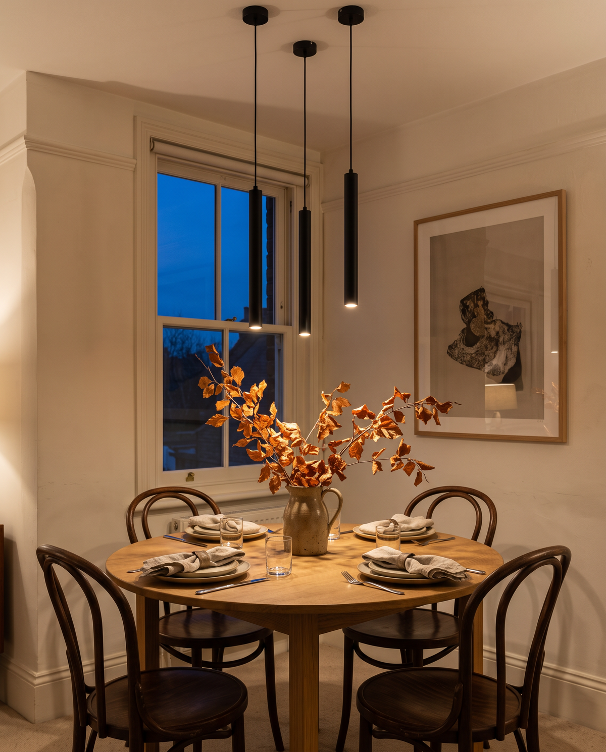 Three Plumb pendants at different heights over a round oak table
