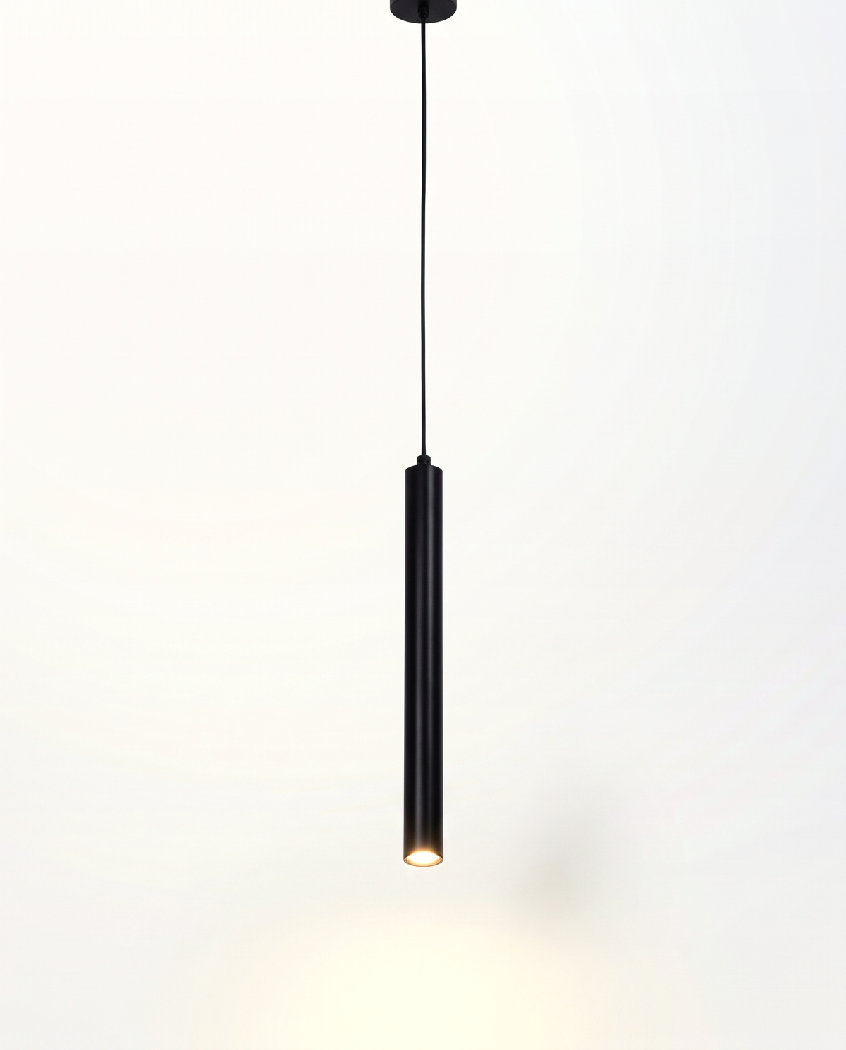 The Plumb Pendant, a slim matt black tube on a fine cord with an LED spot, lit