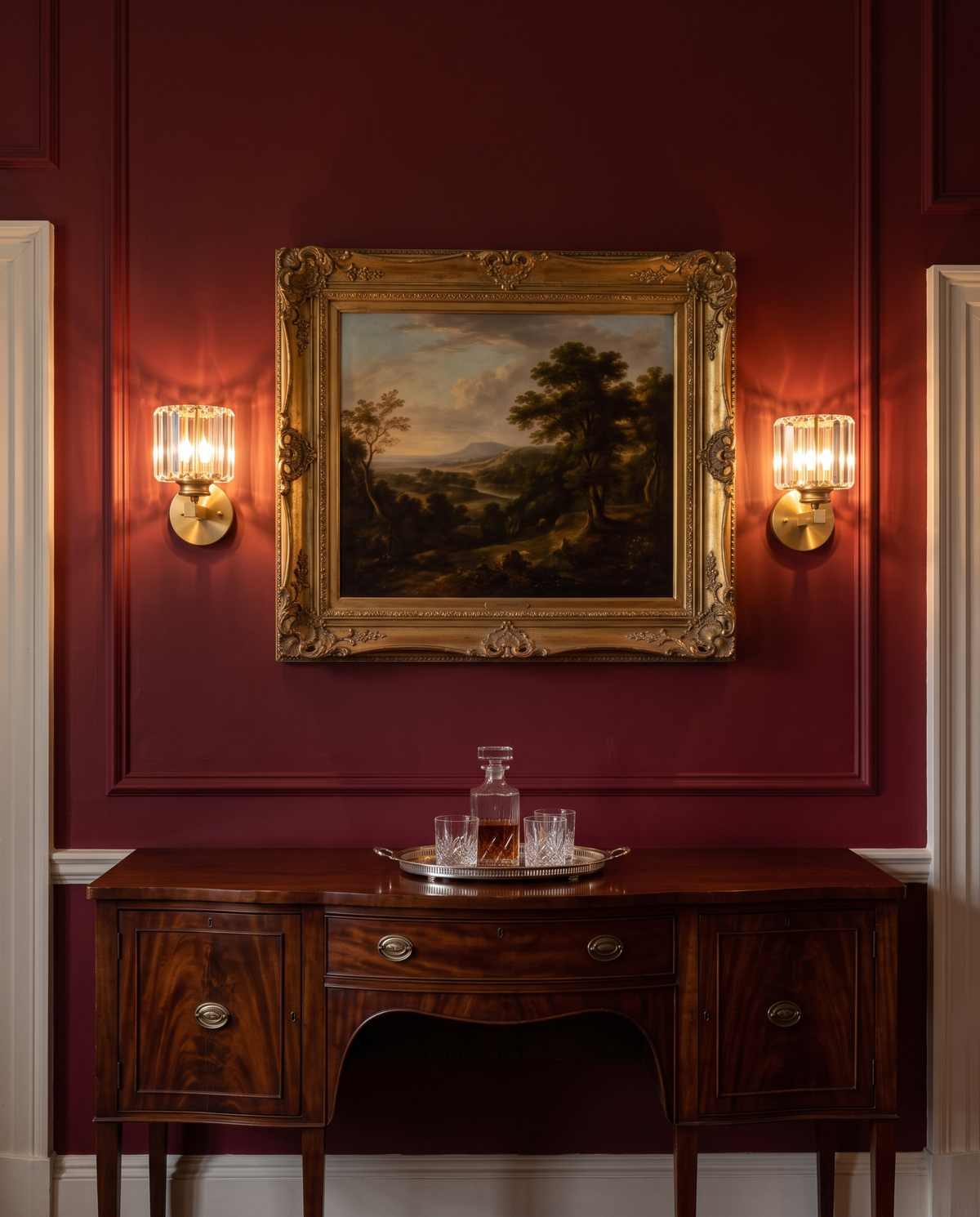 A pair of Prism crystal wall sconces in brass either side of a painting in a red dining room