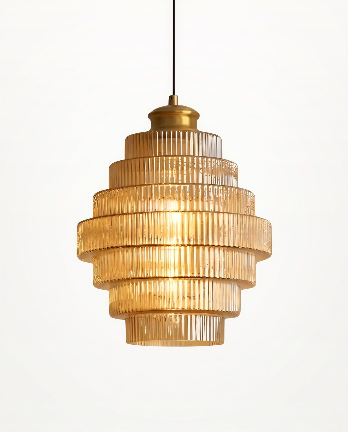 The Skep Pendant in Amber, stacked tiers of ribbed glass under a brass finish cap, lit