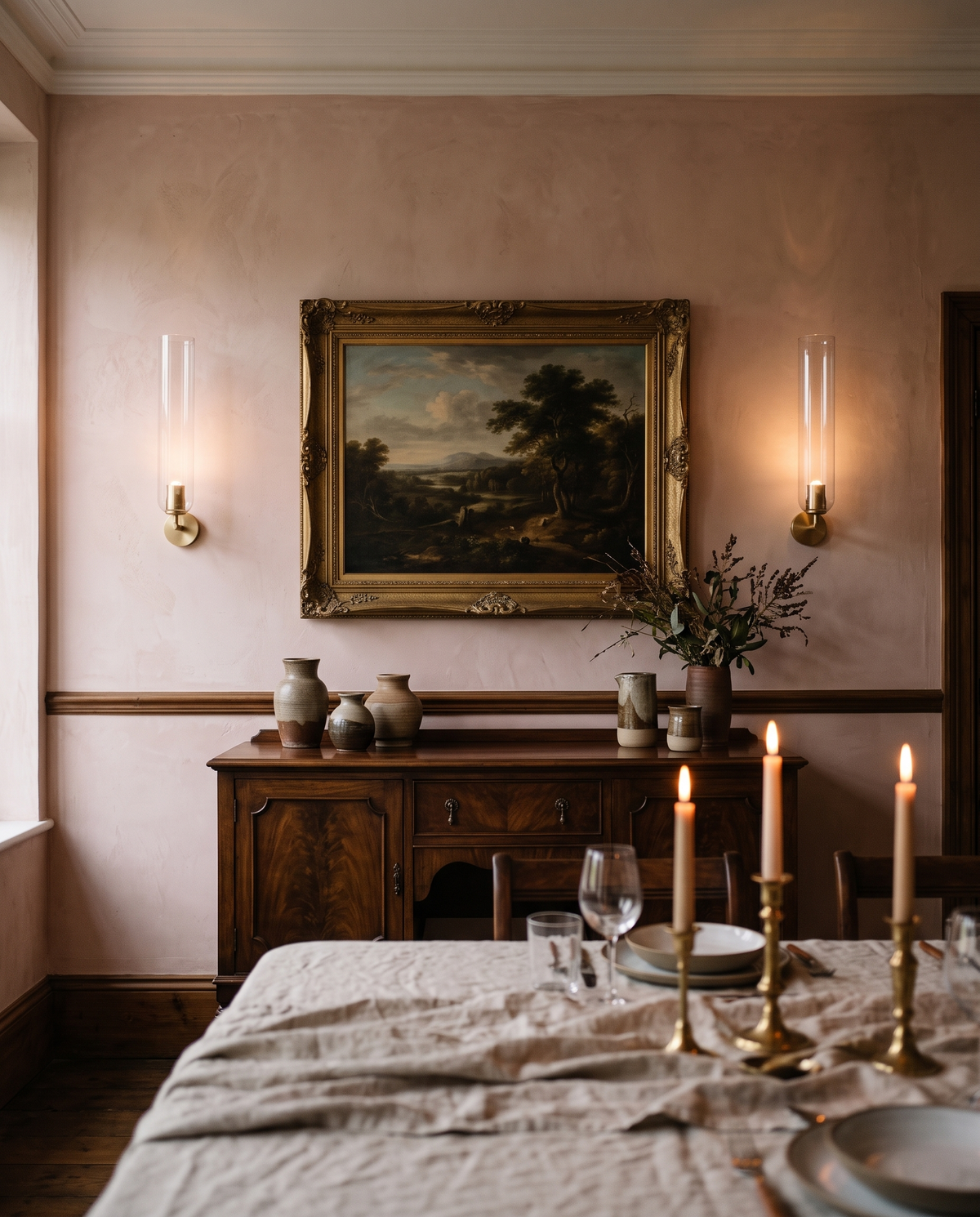 Two Taper wall lights pointing up either side of a painting in a dining room