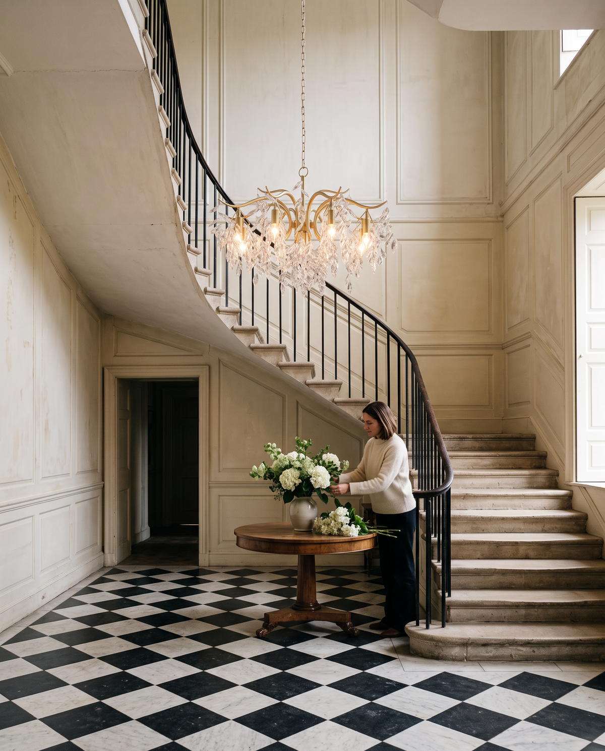 A woman arranging flowers under The Willow in a Georgian entrance hall