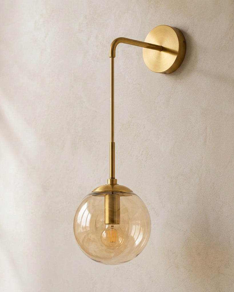 The Lantern, amber glass wall sconce on gold hook arm, mounted on plaster wall — Selden Home product photography