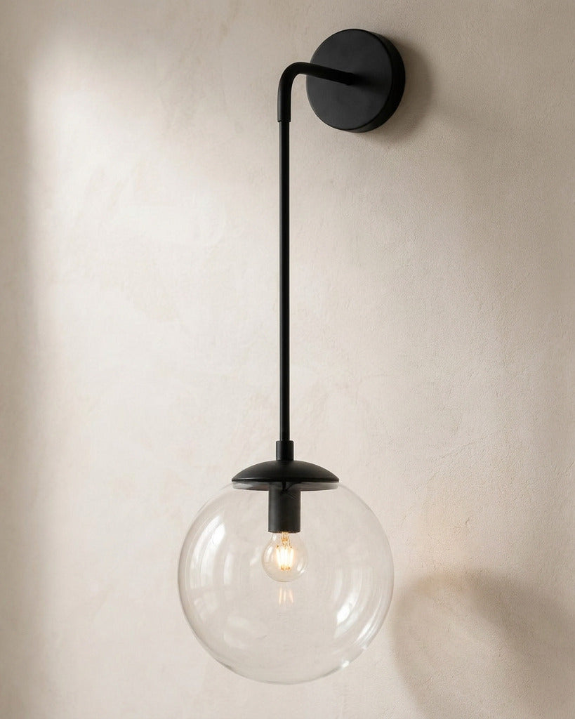 The Lantern, clear glass wall sconce on black hook arm, mounted on plaster wall — Selden Home product photography