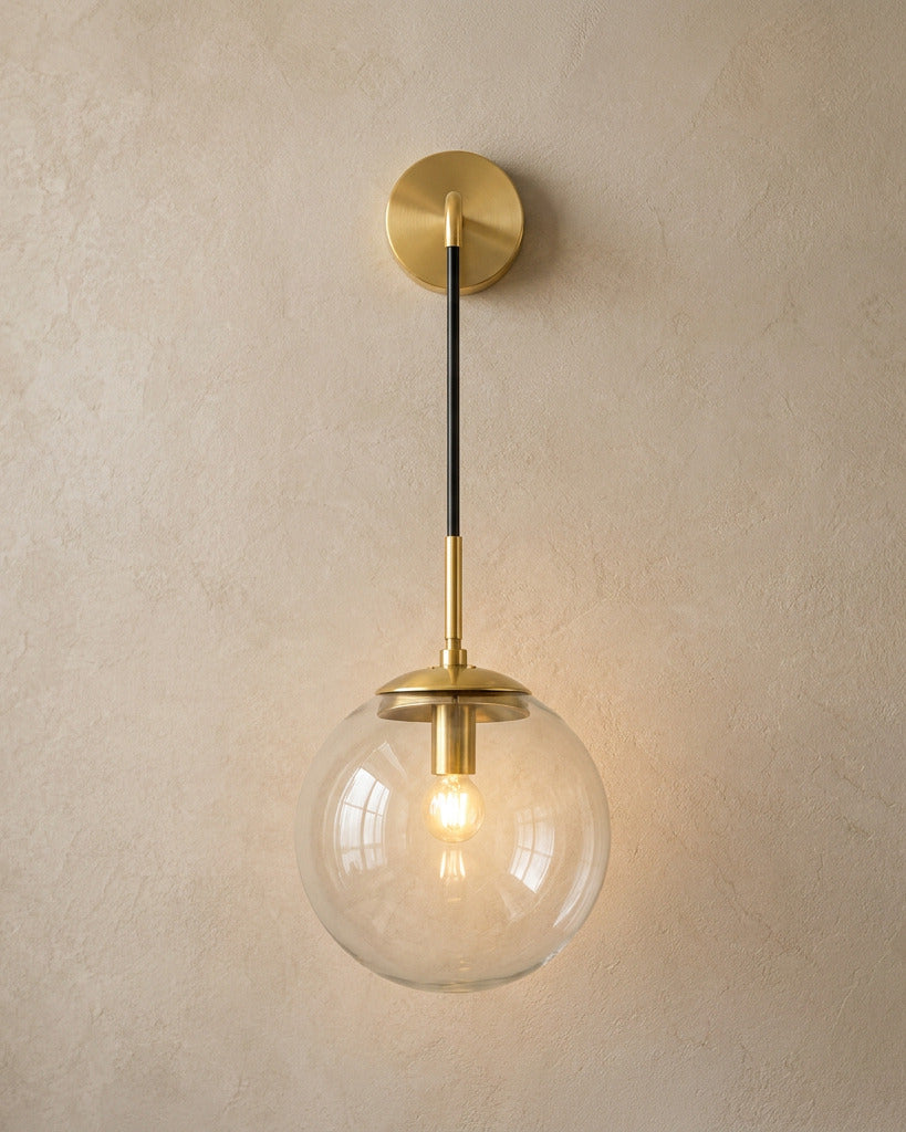 The Lantern, clear glass wall sconce on gold hook arm, mounted on plaster wall — Selden Home product photography