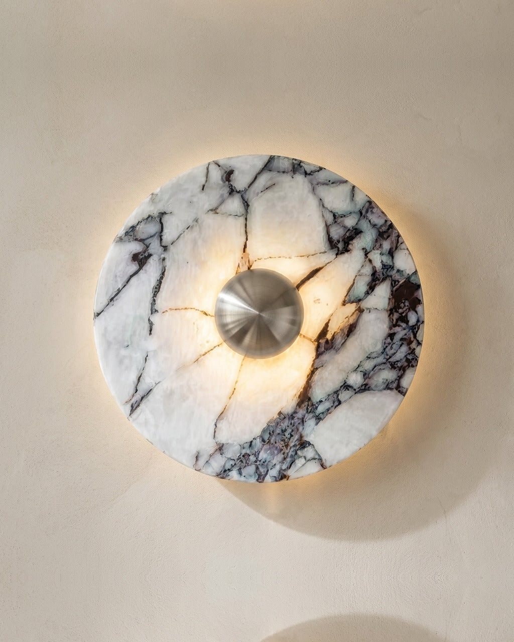 The Orb wall light in silver-tone marble finish, lit, on a lime-washed plaster wall — Selden Home product photography