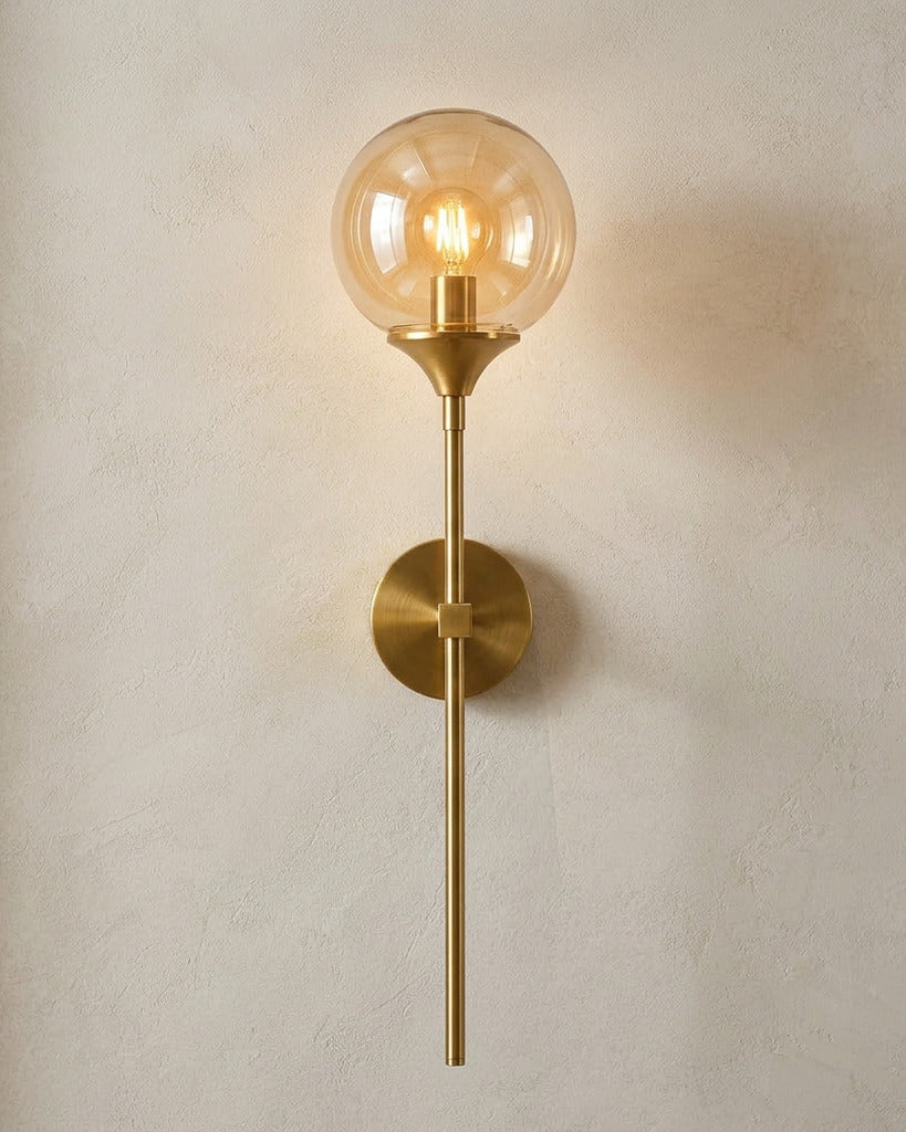 The Reed, gold long-stem wall sconce with amber glass globe, mounted on plaster wall — Selden Home product photography